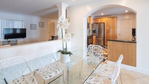 A modern kitchen with stainless steel appliances, a dining area with glass tables and white chairs, and a TV on a stand. - Stunning Lake-Front Villa with Pool & Spa (Pembroke Pines)
