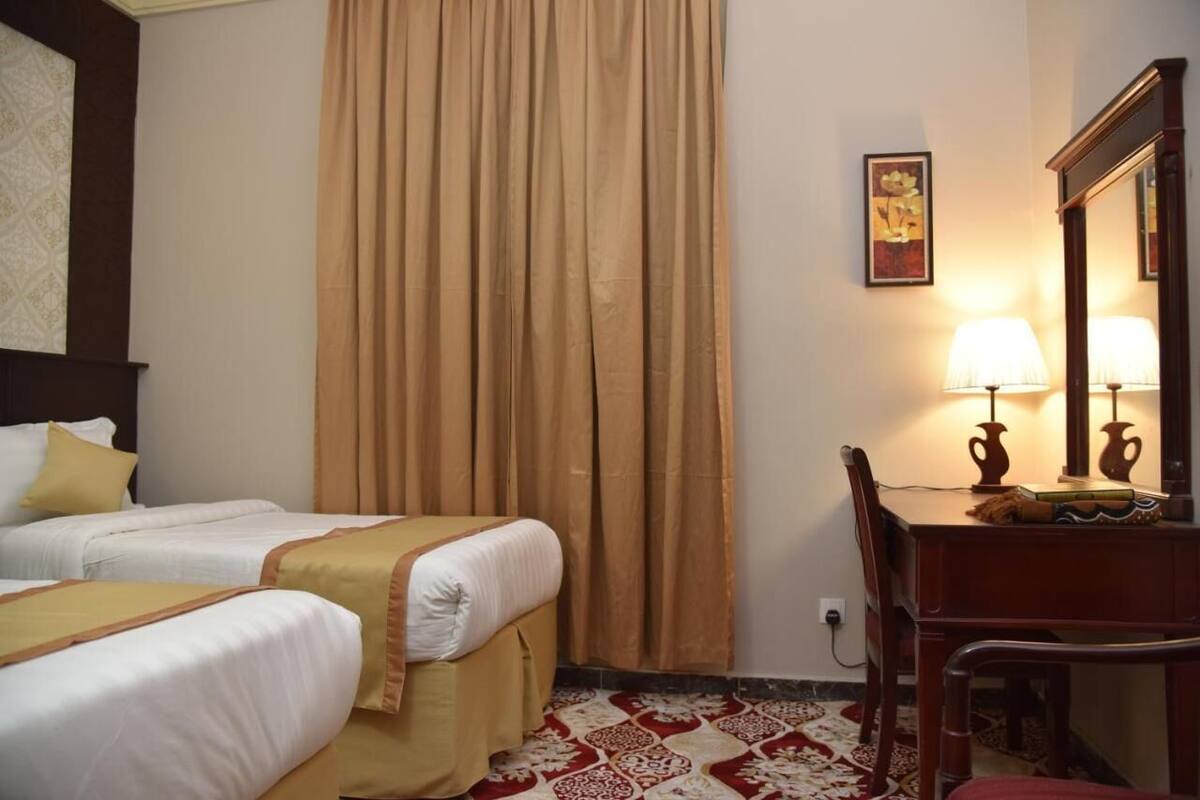 A hotel room with two beds, a desk with lamps, a mirror, and a patterned carpet.