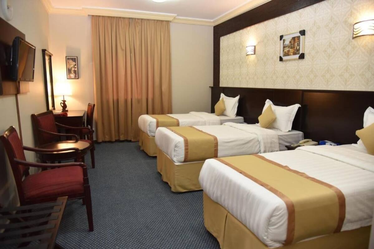A hotel room with three beds, a desk, a chair, and a television.