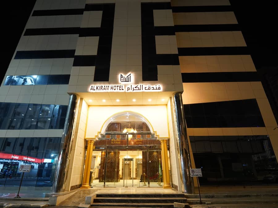 The exterior of the Al Kiram Hotel with a modern design, featuring a prominent entrance with glass doors and a sign above.