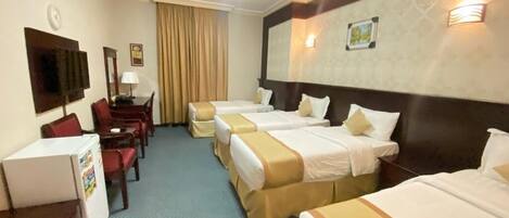 Une chambre d’hôtel avec quatre lits simples, un bureau avec une chaise, une télévision et un réfrigérateur.
