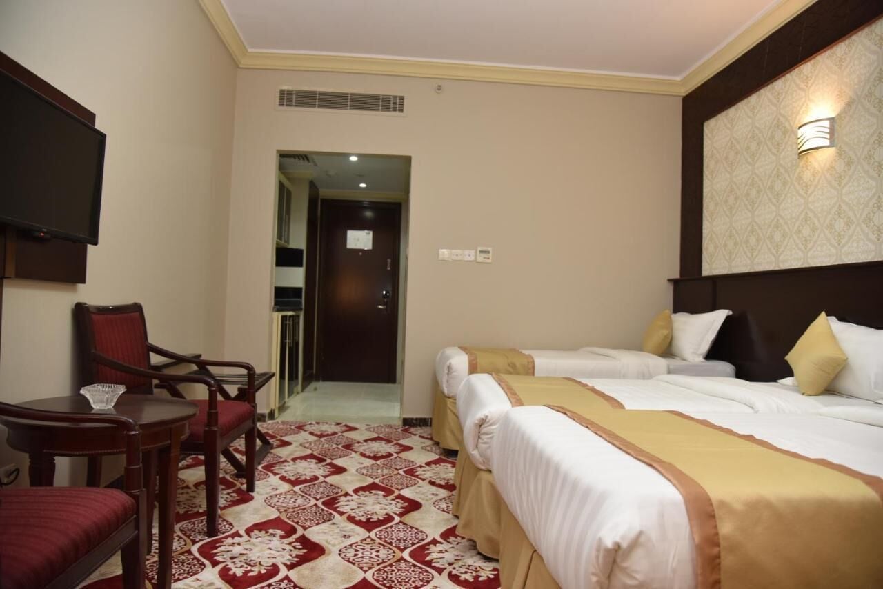 A hotel room with two beds, a TV, a dining table with chairs, and a patterned carpet.
