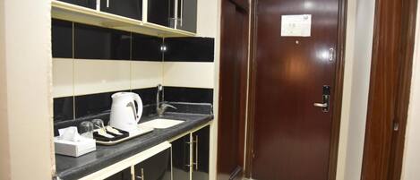 A compact kitchen with a black countertop, a white kettle, and a small sink.