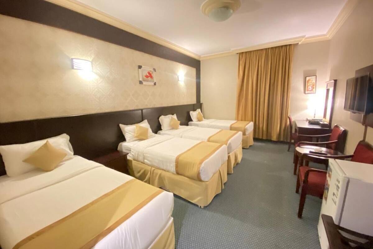 A hotel room with four single beds, a desk, a chair, and a television.
