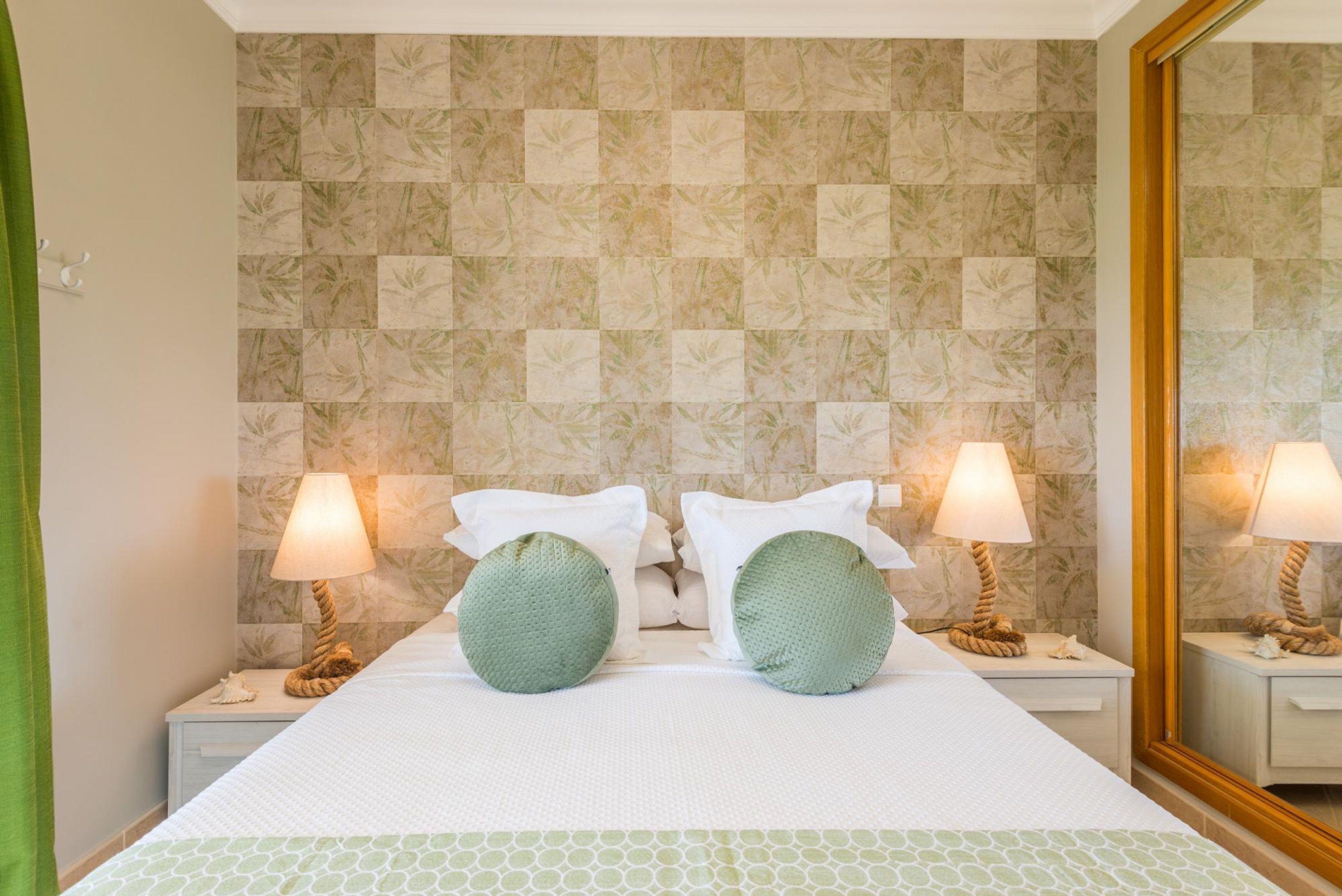 A hotel room with a bed, two nightstands, two lamps, a mirror, and a patterned wall.