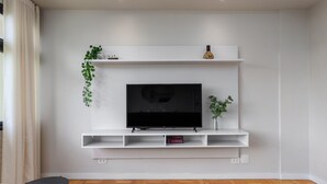 A modern living room with a flat-screen TV mounted on a white wall, wooden flooring, and a small table with two chairs.