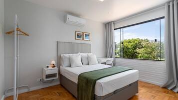 A modern bedroom with a bed, bedside table, and a view of greenery through large windows.