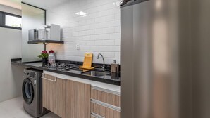 A modern kitchen with a stainless steel refrigerator, a built-in oven, a washing machine, and a wooden countertop.