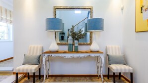 Un área de recepción con una mesa consola, dos sillas, un espejo y una escalera al fondo.