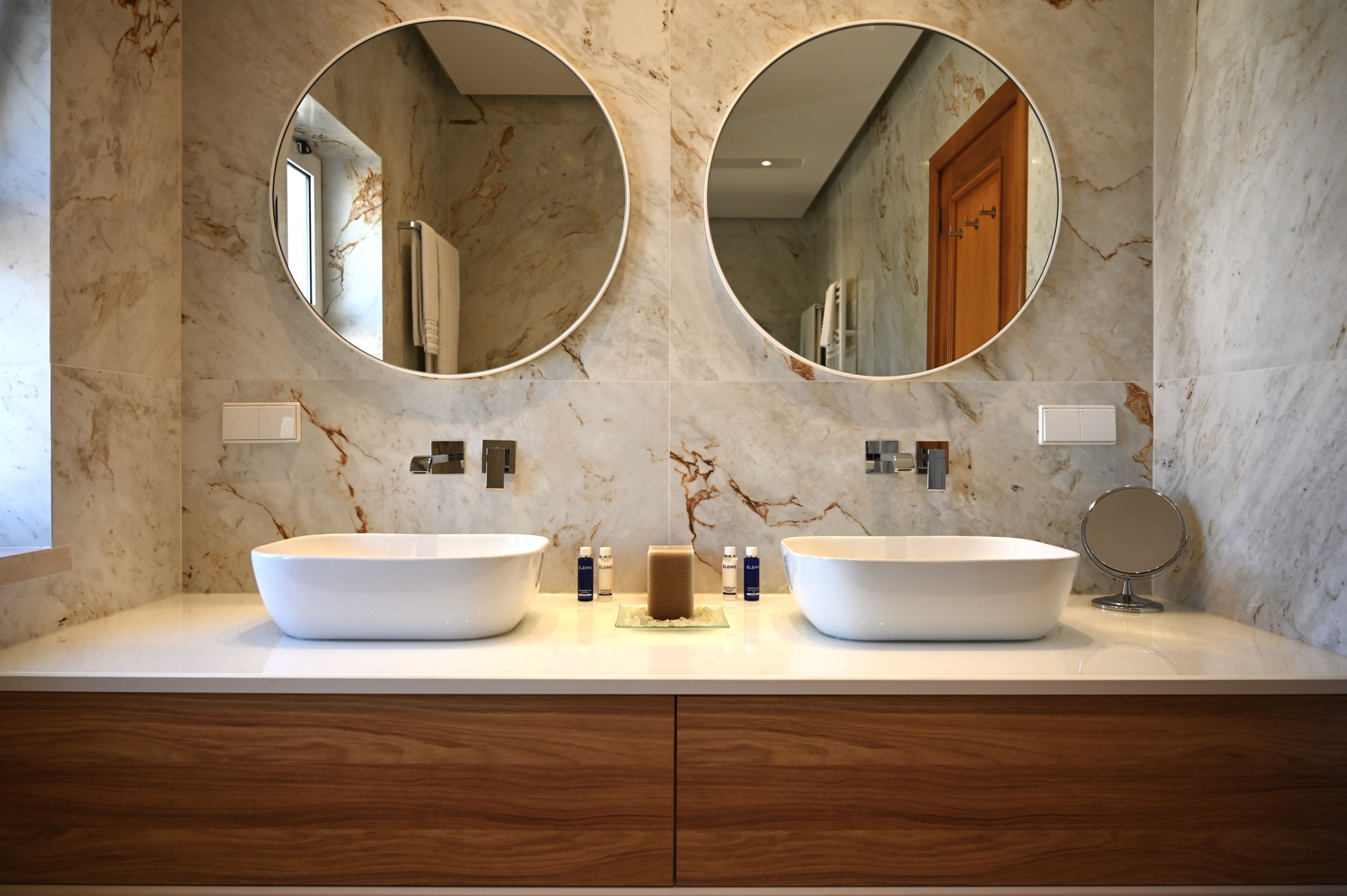 Un baño con dos lavamanos ovalados grandes, un mueble de tocador de madera y dos espejos fijados a la pared.