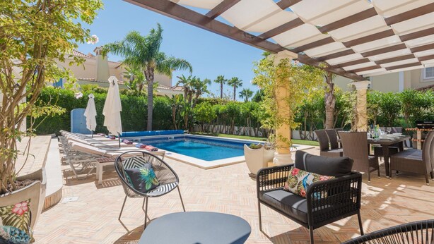 Un área junto a la piscina con sillones de descanso, una mesa y sombrillas.