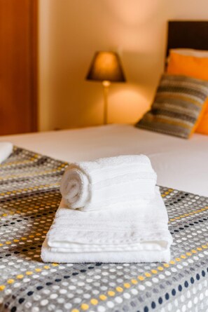 A neatly made bed with a rolled white towel on it, a patterned bedspread, and a lamp in the background. - Quinta do Paiva - Jardins do Vale (Albufeira)