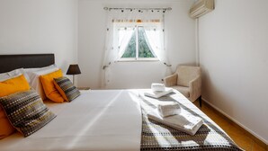 Et hotelværelse med seng, stol, et vindue med gardiner og en aircondition.