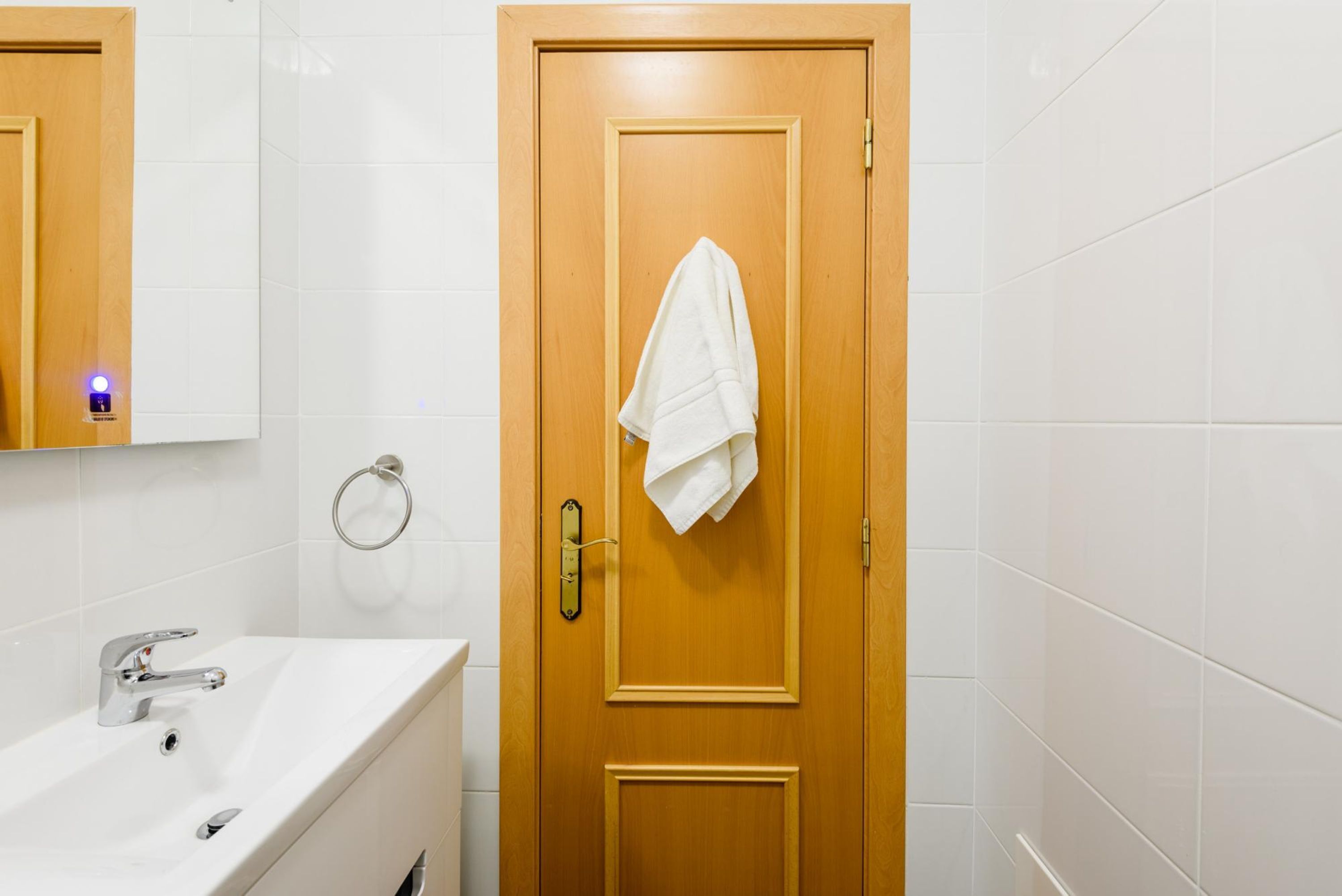 Een badkamer met een houten deur, een witte wastafel en een handdoek aan de deur.