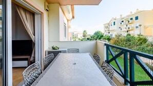 En balkon med et bord, stole, et fjernsyn og udsigt til omkringliggende bygninger.