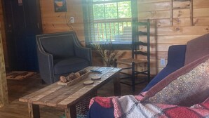 L’intérieur d’un chalet accueillant, avec une cheminée, des murs en bois, un canapé, une table basse et une fenêtre équipée de stores.
