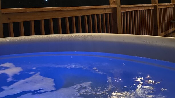 Un bain à remous installé sous une terrasse en bois, illuminé de guirlandes lumineuses.