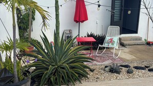 Un área de piscina con una sombrilla roja, una silla blanca con un diseño de pájaro y una mesa roja.