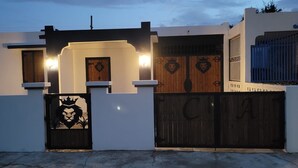 A modern house with a gated entrance, a decorative gate with a lion motif, and a wooden gate with the letters "C A" visible.