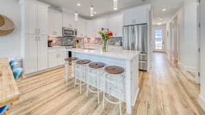A modern kitchen with white cabinets, a central island with stools, stainless steel appliances, and pendant lighting. - Joyful Sound by AvantStay | Walk to the Beach (Panama City Beach)