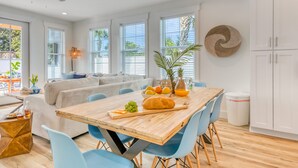 A modern kitchen with a wooden table, blue chairs, and a white cabinet. - Joyful Sound by AvantStay | Walk to the Beach (Panama City Beach)