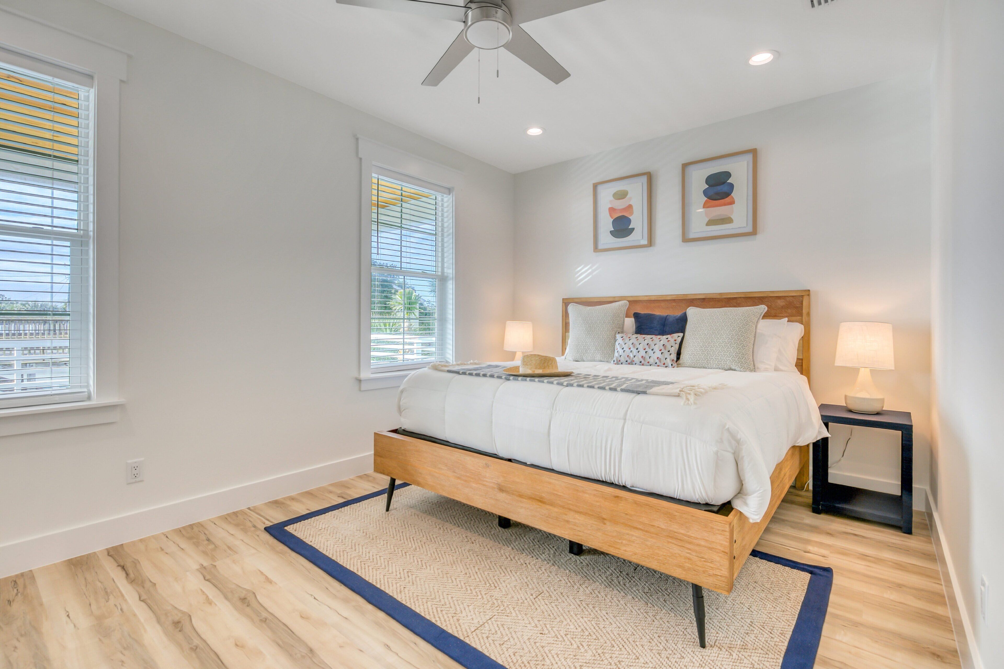 A bedroom with a wooden bed, two bedside lamps, a ceiling fan, and a view of the outside through the window.