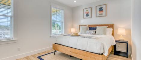 A bedroom with a wooden bed, two bedside lamps, a ceiling fan, and a view of the outside through the window.