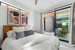 A modern bedroom with a large bed, a wooden headboard, and abstract artwork on the wall.