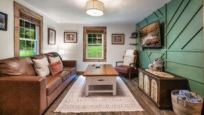 A cozy living room with a wooden coffee table, leather sofa, and a green accent wall. - EV Cottage, Fenced Yard, Pets Free (Sevierville)