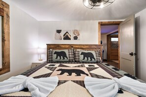A bedroom with a bed featuring a bear-themed quilt, a wooden headboard, and a nightstand with a lamp. - EV Cottage, Fenced Yard, Pets Free (Sevierville)