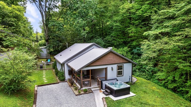 A small house with a covered porch, a hot tub, and a gravel driveway. - EV Cottage, Fenced Yard, Pets Free (Sevierville)