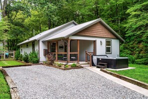 A two-story house with a covered porch, a hot tub, and a gravel driveway. - EV Cottage, Fenced Yard, Pets Free (Sevierville)