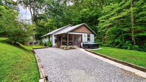 A house with a gravel driveway, a porch, and a large tree in the background. - EV Cottage, Fenced Yard, Pets Free (Sevierville)