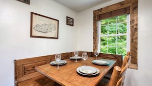 A dining room with a wooden table set for four, two chairs on each side, and a window with a view of greenery. - EV Cottage, Fenced Yard, Pets Free (Sevierville)