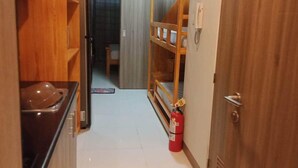 Un pasillo estrecho con armarios de madera, una zona de cocina, una cama litera y un extintor.
