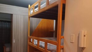 Una cama individual sobre otra con estructura de madera, un colchón blanco y una mesita de noche con lámpara.