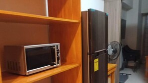 Una cocina con un microondas en un estante, un refrigerador y un armario de madera con vajilla.