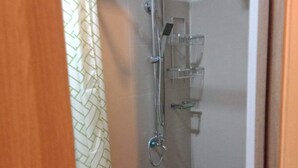 Un espacio de ducha pequeño y cerrado, con cabezal de ducha, ducha de mano y un estante para artículos de aseo.
