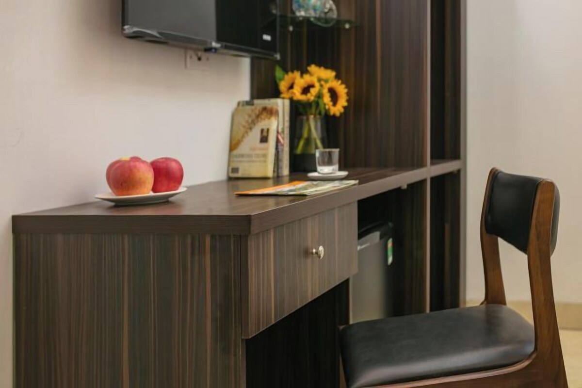 A wooden desk with a black chair, a vase with sunflowers, and two apples on the desk.