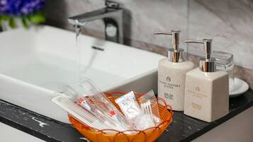 Ein Badezimmer mit einem weißen Waschbecken, einem Wasserhahn und zwei Seifenspendern. Auf der Ablagefläche befindet sich ein Korb mit Pflegeprodukten.