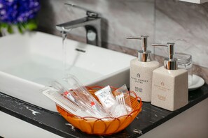 A bathroom with a white sink, a faucet, and two soap dispensers. A basket with toiletries is on the counter. - Hanoi Airport Suites Hostel & Travel (Hanoi)