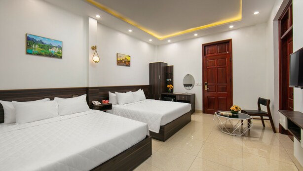 A hotel room with two beds, a desk, a chair, a TV, and artwork on the walls. - Hanoi Airport Suites Hostel & Travel (Hanoi)