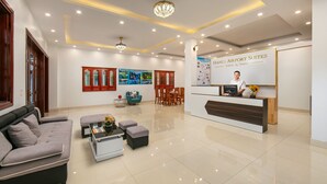 A hotel lobby with a reception desk, seating area, and a large poster advertising hotel services. - Hanoi Airport Suites Hostel & Travel (Hanoi)