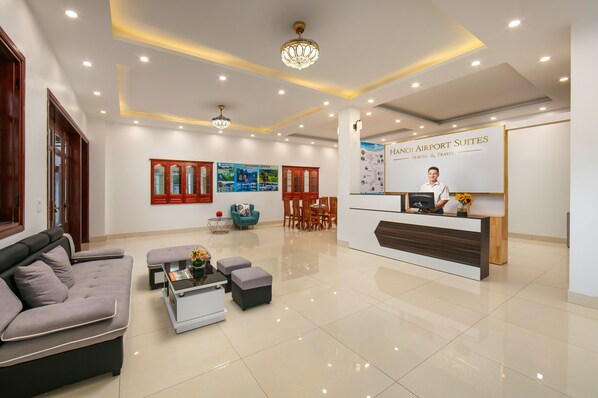 A hotel lobby with a reception desk, seating area, and a large poster advertising hotel services. - Hanoi Airport Suites Hostel & Travel (Hanoi)