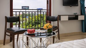 A hotel room with a balcony, a TV mounted on the wall, and a table with a vase of flowers and apples. - Hanoi Airport Suites Hostel & Travel (Hanoi)