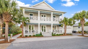 A two-story house with a balcony, surrounded by palm trees and a clear sky.