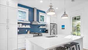 A modern kitchen with white cabinets, a blue backsplash, stainless steel appliances, and a large island with bar stools.