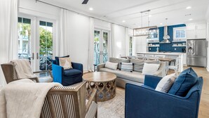 A spacious living area with a sofa, chairs, a coffee table, and a kitchen in the background.