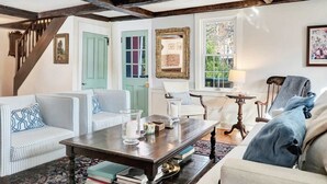 A room with a wooden staircase, a striped sofa, a coffee table, and a chair with a lamp. - Hillside Farmhouse, Updated & Pet-Friendly (Hartford)