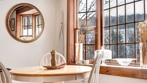 A dining area with a round wooden table, white chairs, a mirror, and a window with a view of trees. - Hillside Farmhouse, Updated & Pet-Friendly (Hartford)